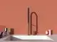 Ideal Standard Küchenarmatur in modernem Design mit einem langen, grauen Griff und goldenen Elementen. Die Armatur ist auf einer weißen Spüle vor einer terrakottafarbenen Wand platziert.